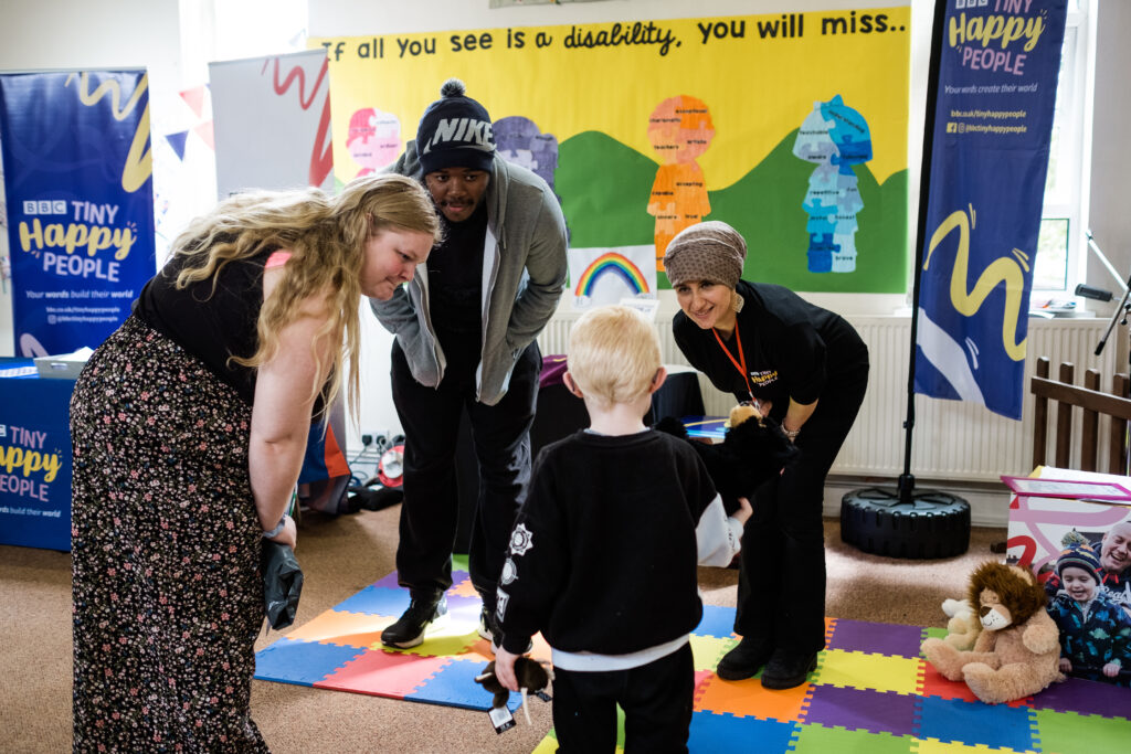 Parents, staff and children stand in a circle playing a game.