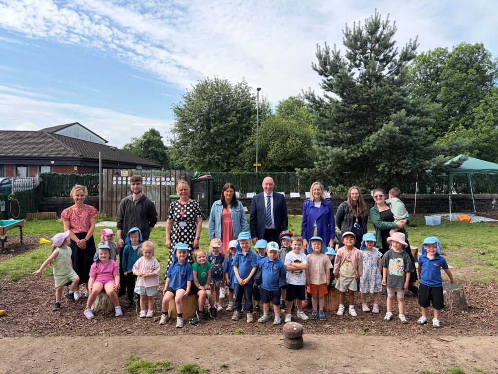 Adults and children outside a children's centre, lined up smiling and looking at the camera