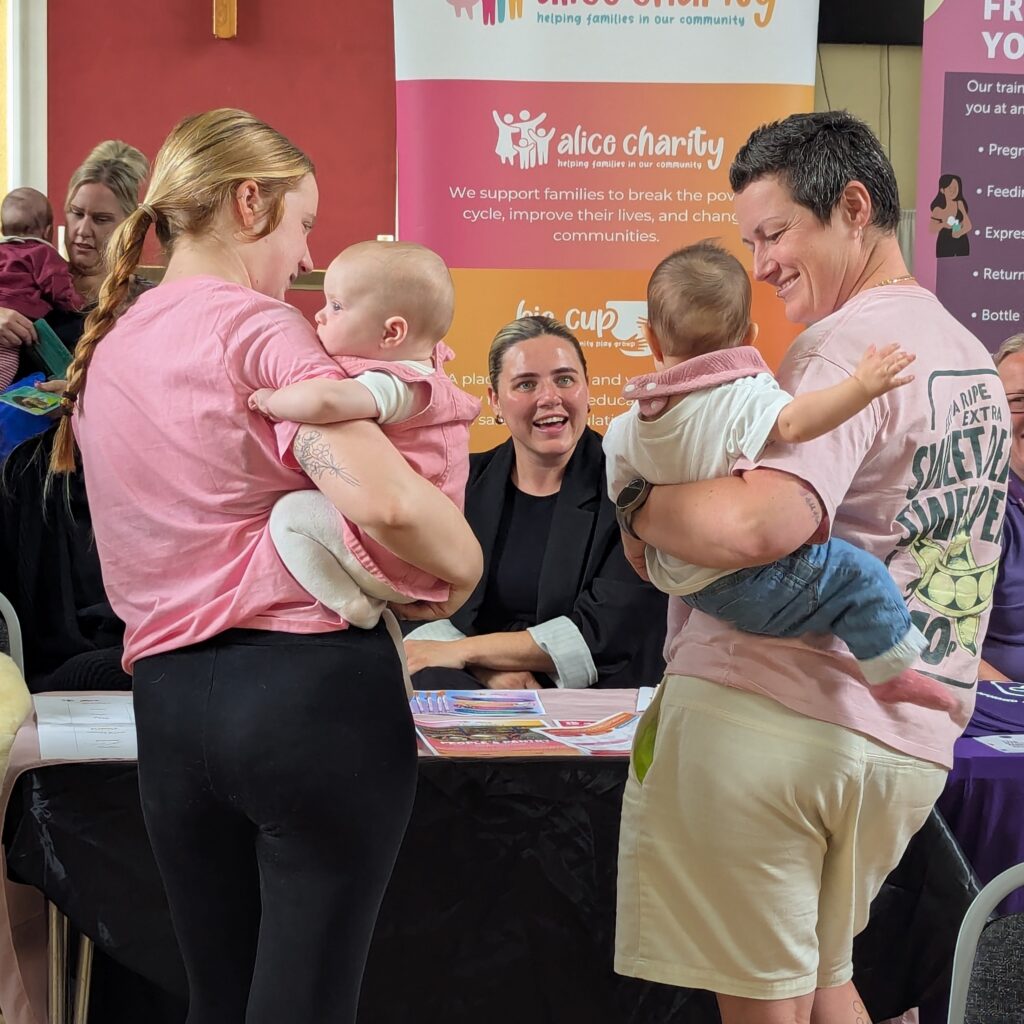 A mum holding a baby and a dad holding a baby stand either side of a stall at the Bumps and Babies event