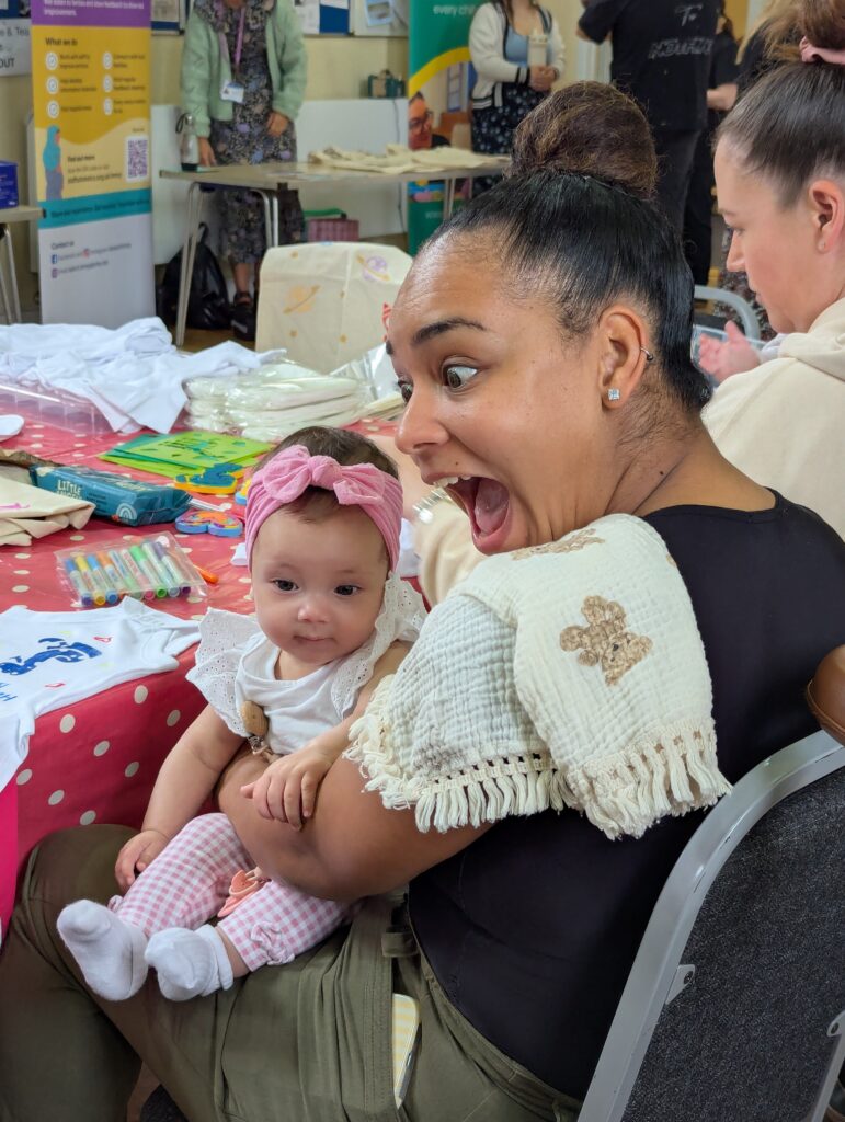 A mum makes a 'wow' face while interacting with the baby on her lap.